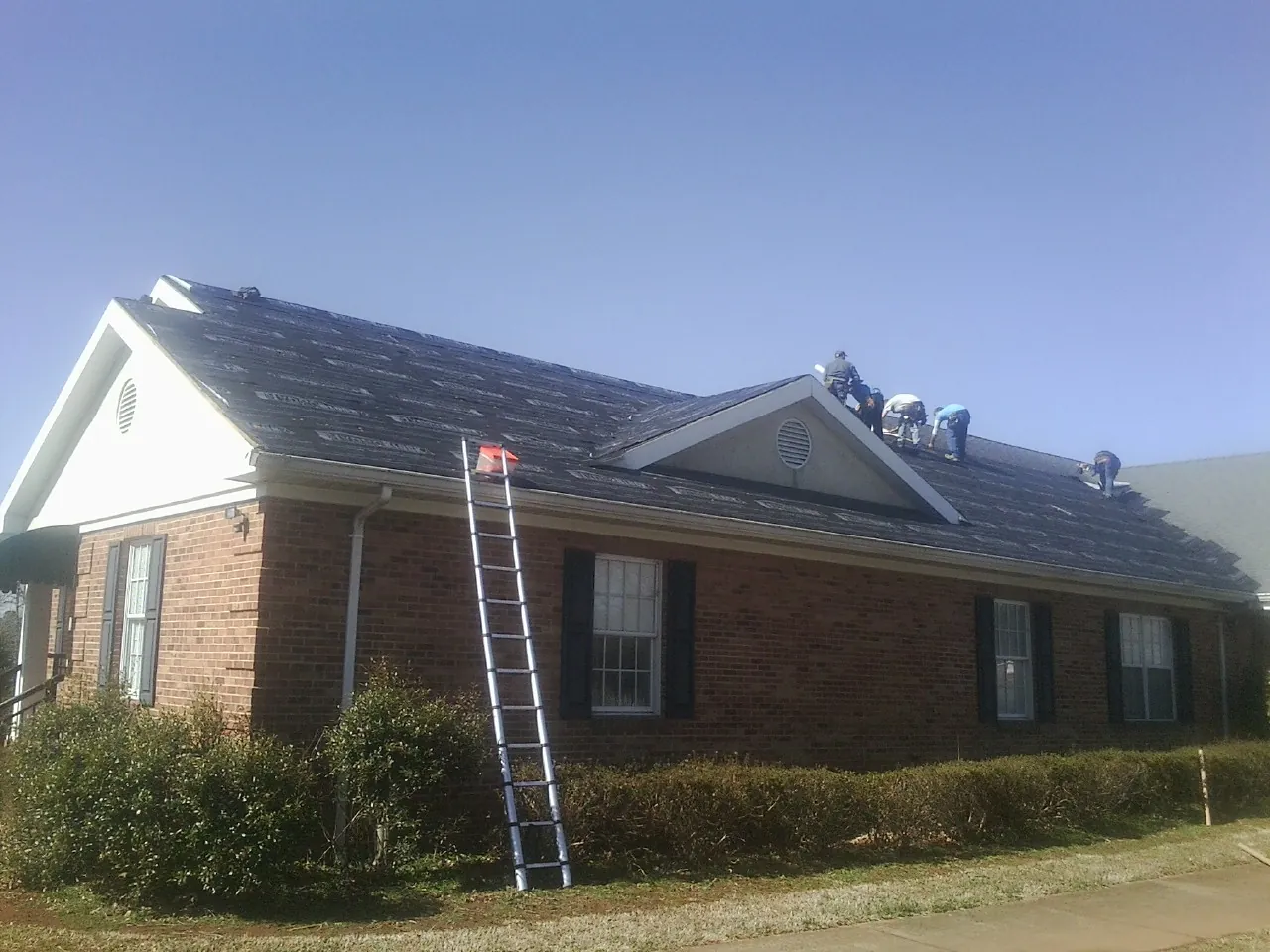 Crew tearing shingles off a brick ranch roof with a ladder set — Emergency Roof Repair work by our crew in Zephyrhills