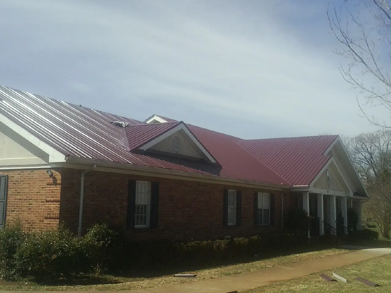 Red metal roof with gabled entries on a long brick building, from a Hail Damage Roof Repair job in Zephyrhills