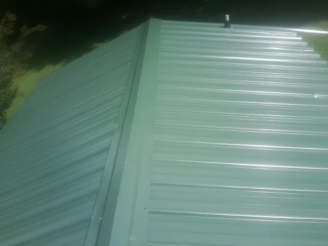 New green metal panels meeting at the ridge of a roof — Flat Roof Repair work by our crew in Zephyrhills