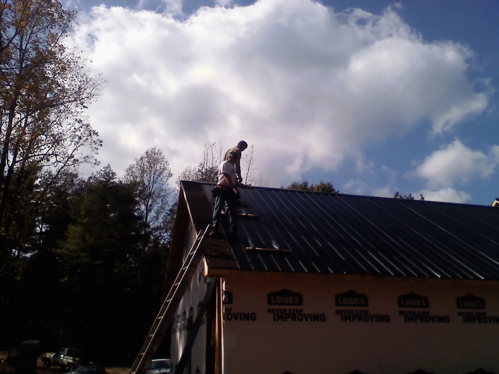 Roofer fastening dark metal panels high against a cloudy sky, from a Roof Inspection job in Zephyrhills