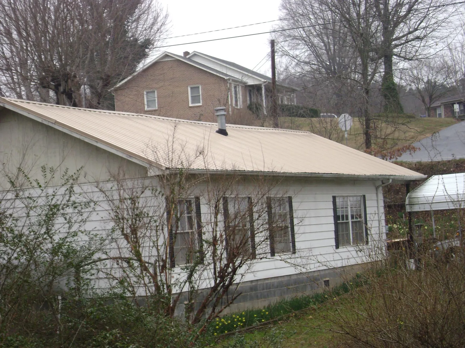Tan metal roof on a white sided house set into a hillside — Commercial Roofing by Roofing Brothers in Zephyrhills
